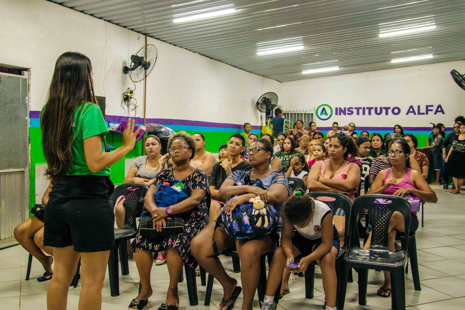 Encontro no salão do Instituto Alfa, com voluntários, colaboradores e famílias reunidos diante da marca da instituição.